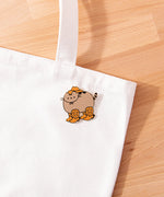 Cowboy Boots Pusheen Pin attached to a white tote bag to show the brown and gray colors on the pin.