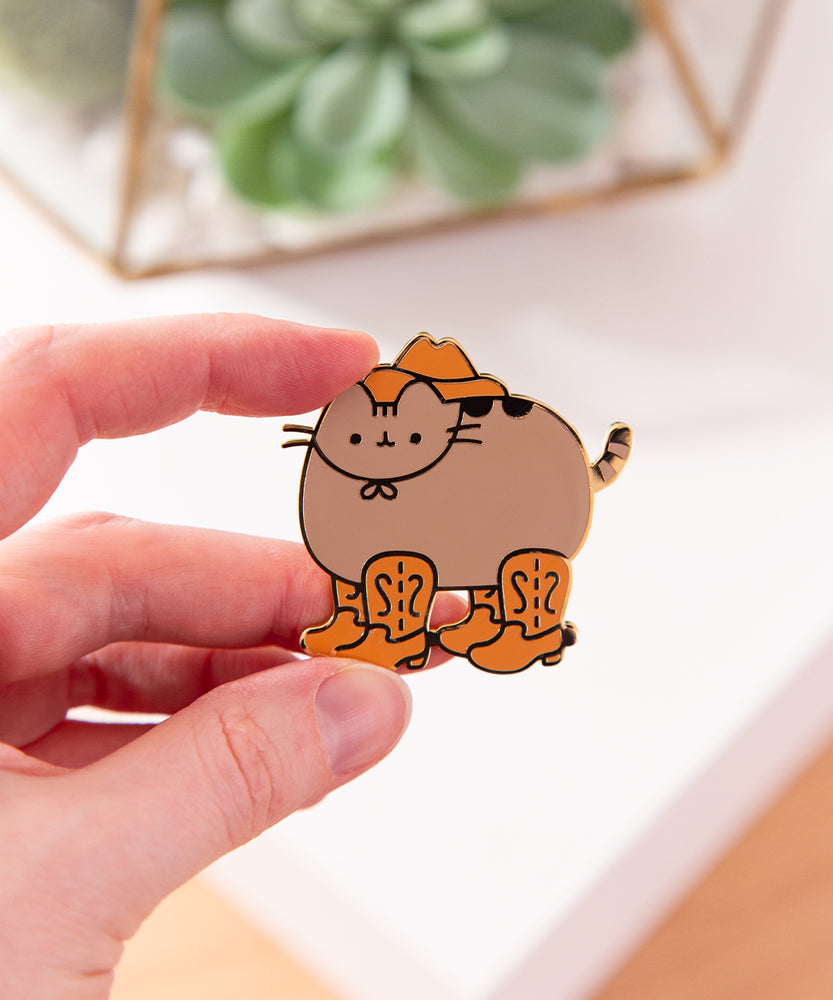 Model holds the Cowboy Pusheen Boots Deluxe Pin to show the scale of the cat-shaped pin with gold plated outline details.