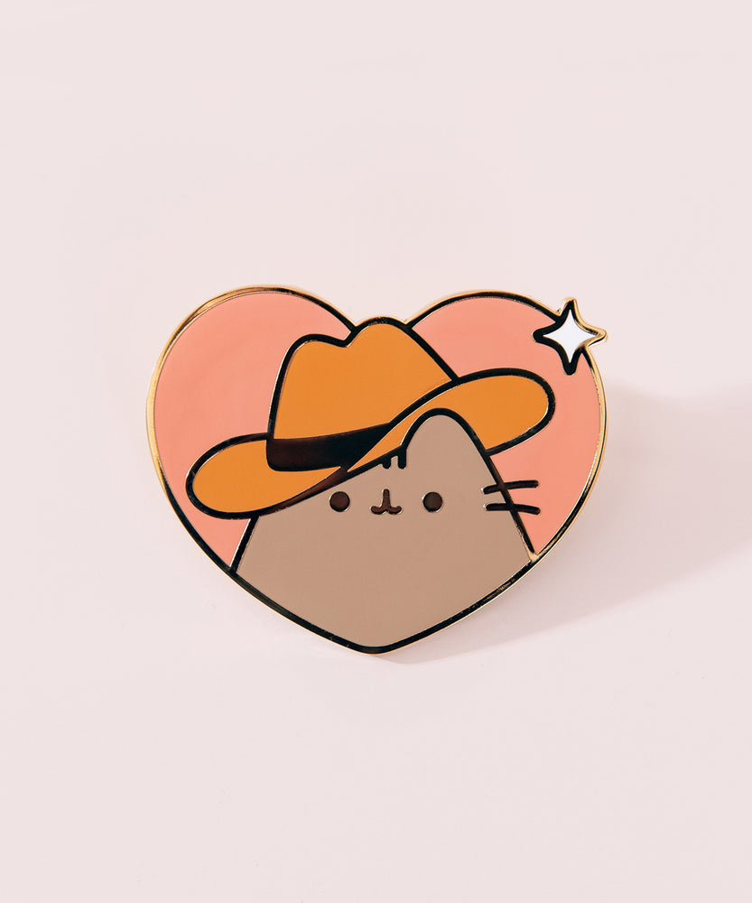 Close-up of Cowboy Pusheen Pin. Pusheen wears a brown cowboy hat while smiling. The middle of the pin has a white sparkle detail on the edge of the heart pin.