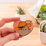 Model holds the Cowboy Pusheen Heart Deluxe Pin to show the scale of the heart-shaped pin with gold plated outline details.