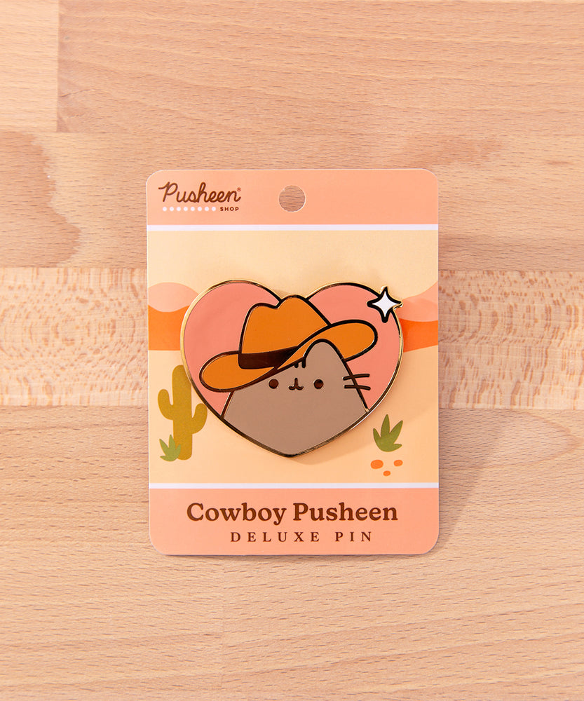 Pusheen the Cat wears a brown cowboy hat and smiles. Pusheen's classic whiskers and head stripes are present on this pin.