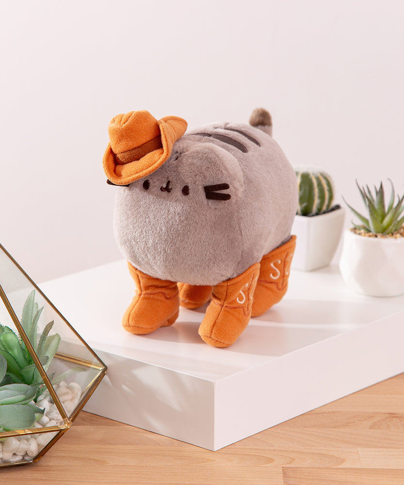 Quarter side view of the Pusheen plush. Pusheen's four paws are wearing cowboy boots.