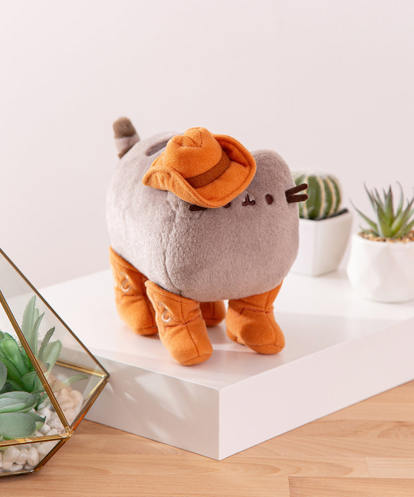 Side quarter view of the Cowboy plush. The cowboy hat is attached to Pusheen's ear and slightly covers her eye and whiskers.