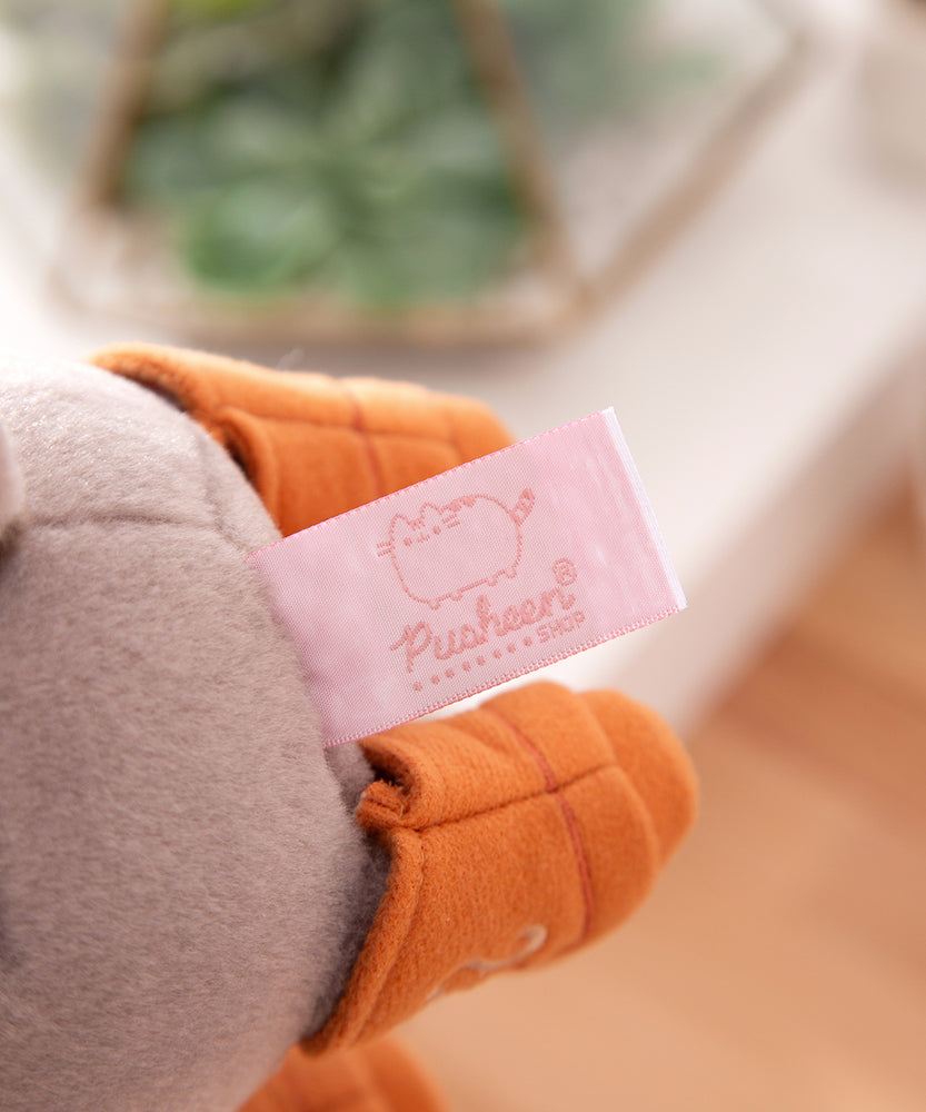 Close-up view of the Pusheen Shop logo tag that is affixed near the bottom of the grey plush.