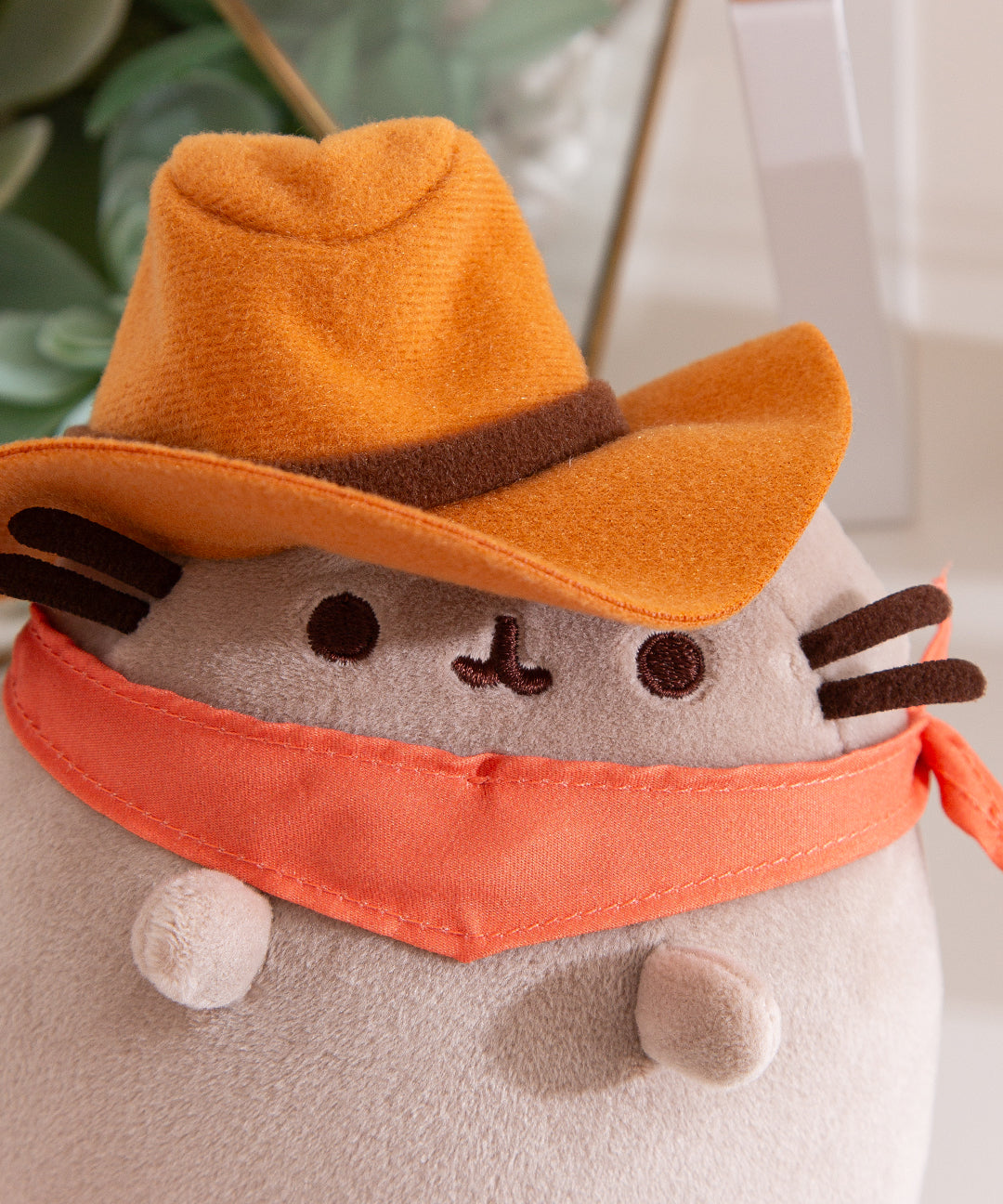 Close-up of Pusheen's face and accessories on the Pusheen Cowboy Squisheen. The brown felt hat has a dark brown piping around the base.