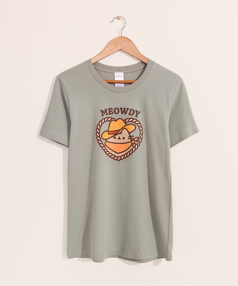 Cowboy Pusheen Tee hangs on a light brown hanger on a light background. The medium green tee shirt has a graphic of Pusheen the Cat wearing a cowboy hat and bandana while surrounded by a rope heart lasso. 