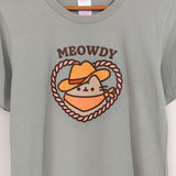 Close-up view of cowboy graphic tee. The phrases above Pusheen graphic in brown colored font is "Meowdy"