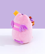Back quarter view of Pusheen Devil’s Food Cake plush. This view shows Pusheen’s back stripes, plush purple wings, and brown cake peeking out the side.  