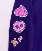 Close-up view of right sleeve of the Halloween Pusheen long-sleeve tee. The graphic running down the sleeve features three icons: a pink whipped frosting dollop, a purple and pink skull, and yellow sparkles that are all outlined in purple and white.  