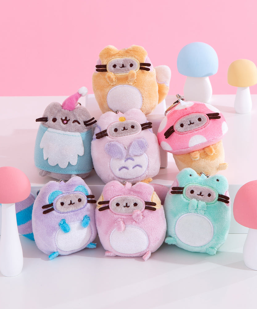 A close-up of the Pusheen Surprise Plush packaging. The front of the packaging features Pusheen as an enchanted raccoon in front of log stump, acorn, mushroom, and rainbow. The packaging says that these Surprise Plush are mini plush. 