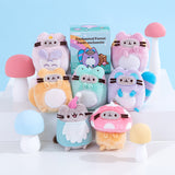Front view of Pusheen Enchanted Forest Surprise Plush assortment. Plush keychains sit on multi-level white pedestal in front of a light blue background. Keychains feature forest friends including a owl, squirrel, fox, frog, raccoon, gnome, and mushroom. Accompanying the seven curious creatures is the mystery box packaging for the Enchanted Forest Surprise Plush. 