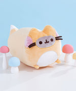 Right side view of the fox Pusheen plush. The orange, white, pink, and grey long plush is surrounded by white, blue, pink, and yellow mini mushrooms. The brown whiskers of the plush extend off of the front of the plush body. 