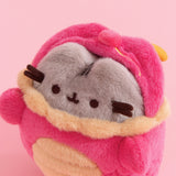 Top aerial view of Dragon Pusheen plush with dragon hood off. Pusheen's fluffy grey ears and brown head stripes can be seen with the hood drawn back.