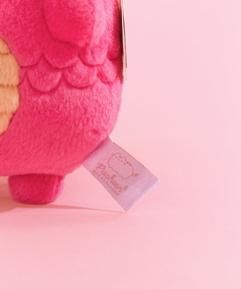 Close-up view of white and pink Pusheen Shop logo tag on the dragon plush.