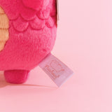 Close-up view of white and pink Pusheen Shop logo tag on the dragon plush.