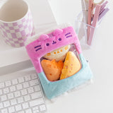 Gamer Pusheen Bag of Chips Plush sits on a white desktop. The pink and blue two-toned bag has a see-through window where the three yellow triangle plush reside.