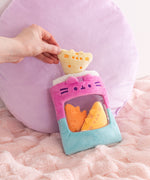 Model holds one of the chip inspired plush above the purple and blue plush bag that has Pusheen's face embroidered above the see-through window.