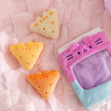 Three triangle plush in a range of yellow colors sit next the the plush bag they come in. Each chip plush has Pusheen's two ears extending off the plush and three stripes embroidered between the ears.