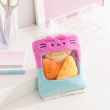 Pusheen Gamer Chips Plush its on a white desktop. The bag features white ribbed edged details on the top and bottom of the  two-toned blue and purple bag.