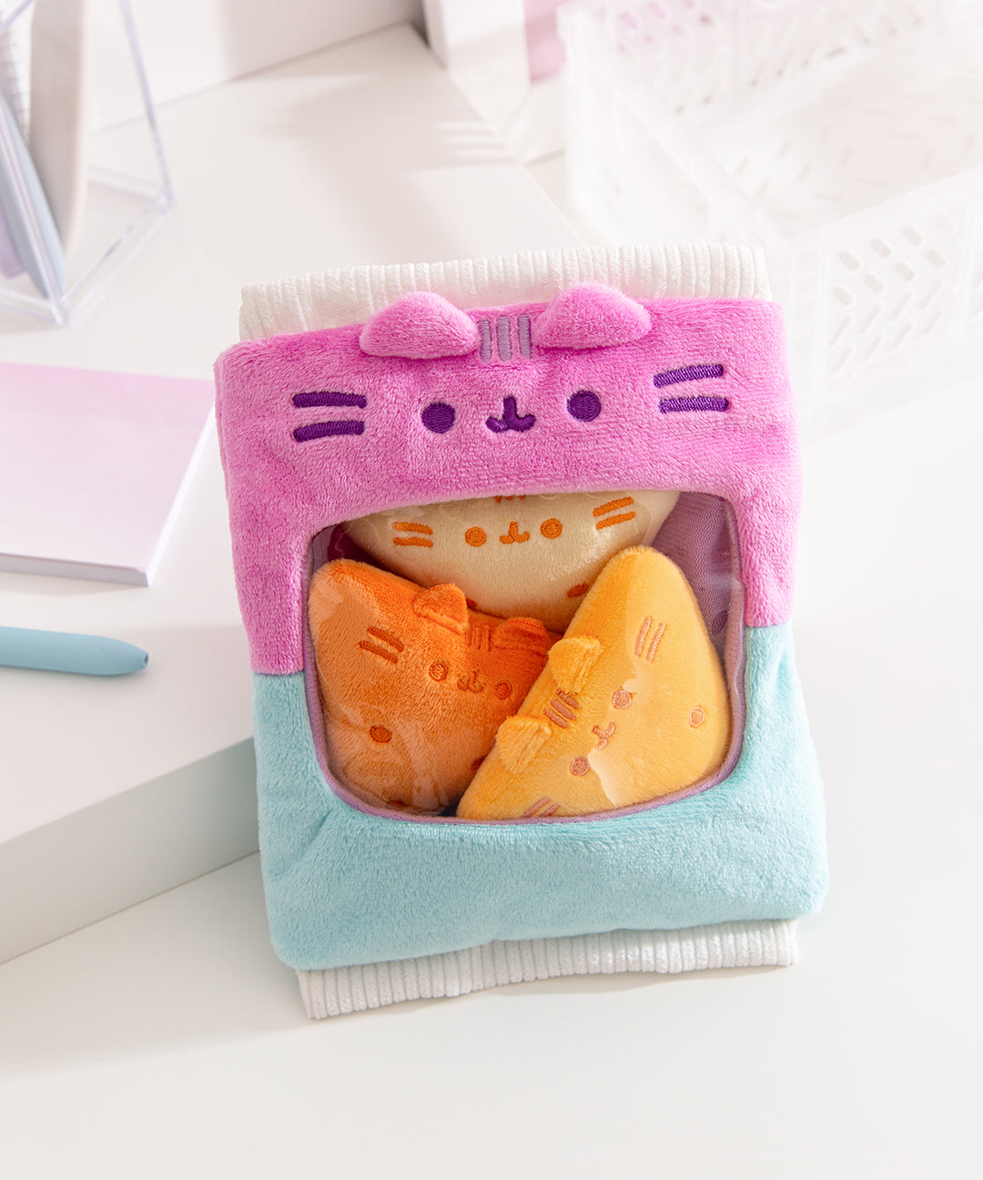 Gamer Pusheen Bag of Chips Plush sits on a white desktop. The plush bag with see-through window holds three triangle plush chips that mimic tortilla chips.