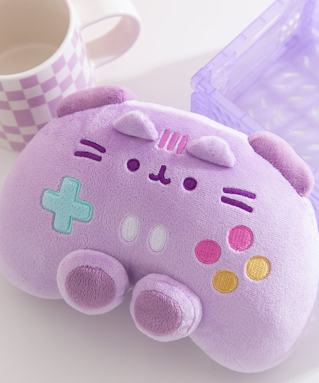 Close-up of the embroidery detail on the gaming controller plush toy. teal, white, pink, and yellow controller buttons are located near the middle bottom of the plush.