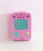 Front view of the pink rectangular shaped plush that mimics the look of a vintage gaming console. At the top of the plush toy, Pusheen's face is embroidered in dark purple while her three head stripes are embroidered in a medium purple color between her two plush ears. 