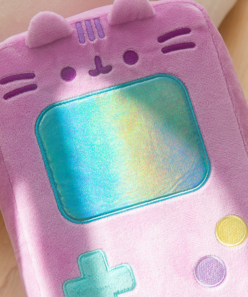 Gamer Pusheen Handheld Console Plush lies on a white surface. Pusheen the Cat takes the form of a pink retro gaming console with a large blue screen and buttons near the bottom of the plush.