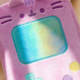 Sunlight shines on the blue rectangular screen of the retro handheld console plush. 