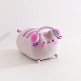 Side quarter view of the gaming squisheen. Pusheen the cat lazes while wearing a pair of multi-colored pastel headphones.