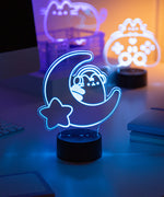 Neon light lamp shaped like a on a crescent moon with a star, glowing on a desk.