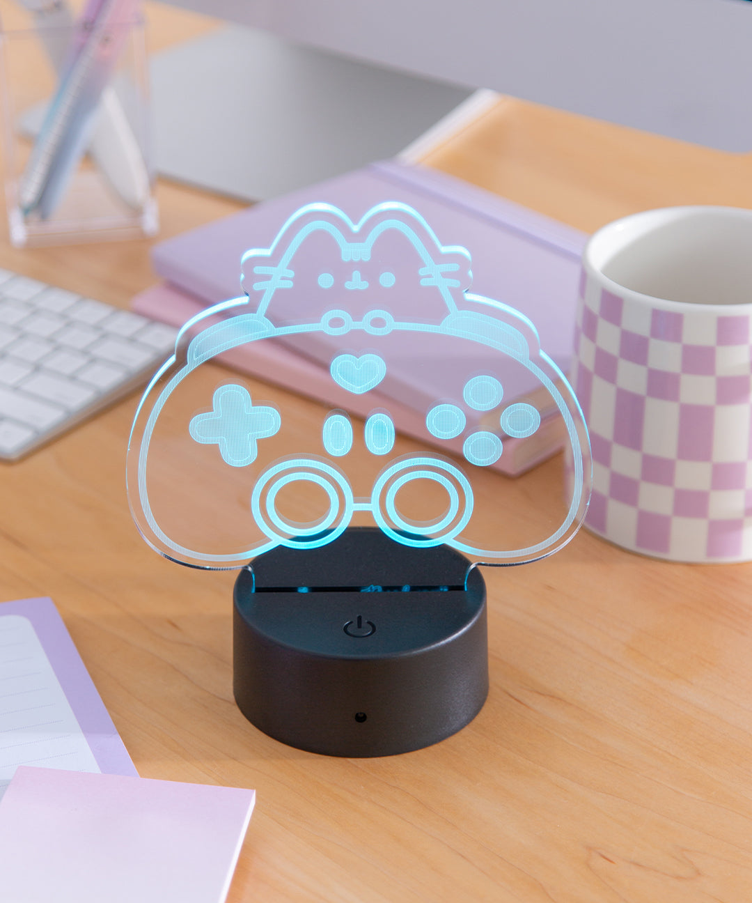 Gamer Pusheen Otaku Lamp shows Pusheen the Cat peeking over a gaming controller. The lamp is shown in daylight to demonstrate the LED light. 
