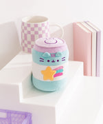Pusheen the Cat takes the form of a blue, white, and purple energy drink can with purple facial embroidery details and a yellow, blue, purple, and pink shooting star that is embroidered on the front of the plush. 