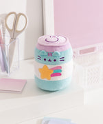 Quarter side view of the can shaped plush toy. Pusheen the Cat's three head stripes are embroidered in a purple color that matches the lid color of the can. The stripes are placed between the triangle shaped ears that extend off the front of the plush.