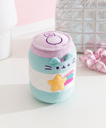 Pusheen Gamer Plush sits on a white surface. The cylinder shaped toy has a pastel blue and purple color palette. 