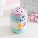 Pusheen Gamer Plush sits on a white surface. The cylinder shaped toy has a pastel blue and purple color palette. 