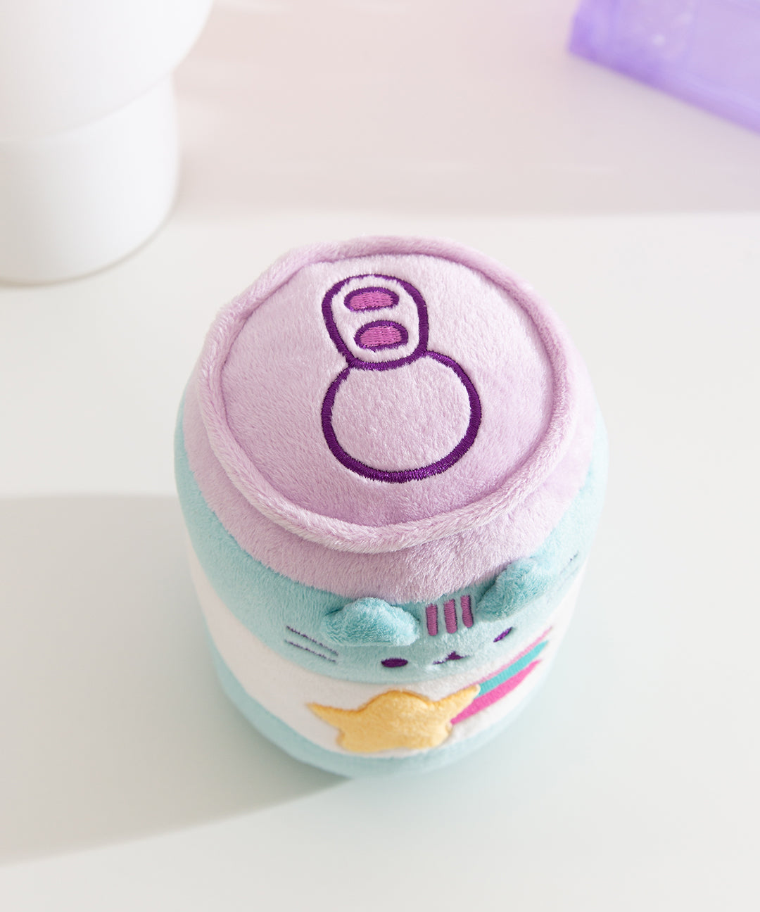Aerial view of the top of the cylinder shaped plush. A purple pop tab is embroidered on the top to emulate an actual energy drink can.