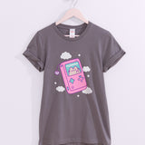 Handheld gaming console printed on a grey tee with the short sleeves rolled up that hangs on a light pink hanger. 