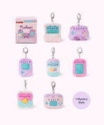 Front view of Pusheen Gamer Surprise Plush assortment. Pusheen the Cat has taken the form of seven miniature video gaming-inspired plushes. At the top left is the packaging box for the Pusheen Gamer surprise plush. The bottom right corner has a burst with the words “1 Mystery Design” indicating eight possible miniature plush keychains are available. 