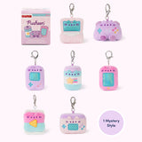Front view of Pusheen Gamer Surprise Plush assortment. Pusheen the Cat has taken the form of seven miniature video gaming-inspired plushes. At the top left is the packaging box for the Pusheen Gamer surprise plush. The bottom right corner has a burst with the words “1 Mystery Design” indicating eight possible miniature plush keychains are available. 