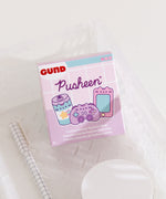 A close-up of the Gamer Pusheen Surprise Plush packaging. The front of the packaging features Pusheen as various gaming characters including a striped energy drink, purple controller, and pink handheld gaming console. The packaging says "Pusheen Gamer Surprise Plush."