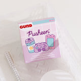 A close-up of the Gamer Pusheen Surprise Plush packaging. The front of the packaging features Pusheen as various gaming characters including a striped energy drink, purple controller, and pink handheld gaming console. The packaging says "Pusheen Gamer Surprise Plush."