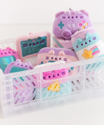 Front view of Gamer Pusheen Surprise Plush assortment. Pusheen the Cat has taken the form of seven miniature gaming accessories in plush keychain form. The gaming blind box plush have a pastel color palette including pinks, purples, blues, and yellows. 
