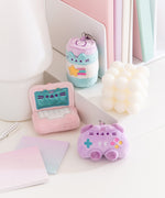 Energy drink, laptop, and controller mini keychains sits on a desktop. The collection of miniature plush have a light pink, purple, and blue color palette.  