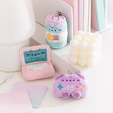 Energy drink, laptop, and controller mini keychains sits on a desktop. The collection of miniature plush have a light pink, purple, and blue color palette.  