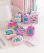 Gamer Pusheen Surprise Plush miniature plush keychains sit on a desktop. The seven blind box plush are accompanied by the box they come in. 