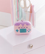 Close-up of the gaming console keychain plush. The light pink plush has Pusheen the Cat's facial features embroidered on the front along with various gaming buttons. 