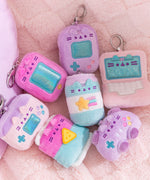 Gamer Pusheen Surprise Plush lie on a plush blanket. The keychain plush are mini figures of gaming consoles, laptops, and gaming snacks. 