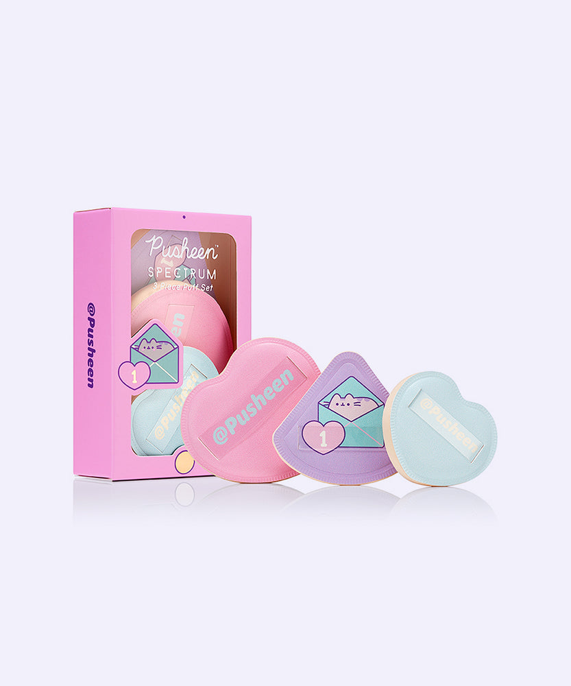 Gamer Pusheen 3-Piece Puffs Set next to its packaging. The pink, purple, and light blue makeup puffs have a cushion material on one side while the other side has a loop for the user to comfortably use the makeup puffs. 