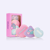 Gamer Pusheen 3-Piece Puffs Set next to its packaging. The pink, purple, and light blue makeup puffs have a cushion material on one side while the other side has a loop for the user to comfortably use the makeup puffs. 