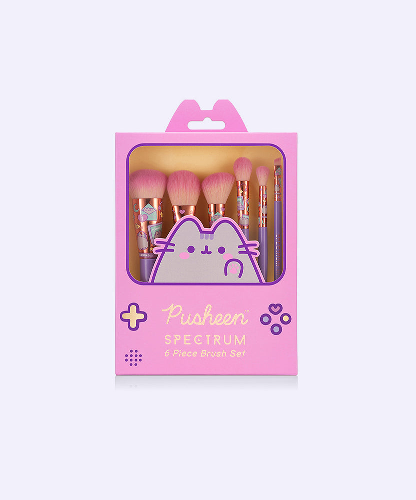 Front view of Pusheen Makeup Brush Set packaging. The pink rectangular box imitates a classic gaming device with an open window to view the tops of the 6-piece makeup brush set enclosed.   